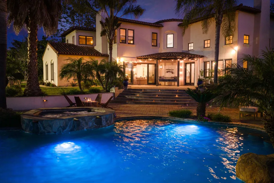 Lit pool and spa with the home behind it at night