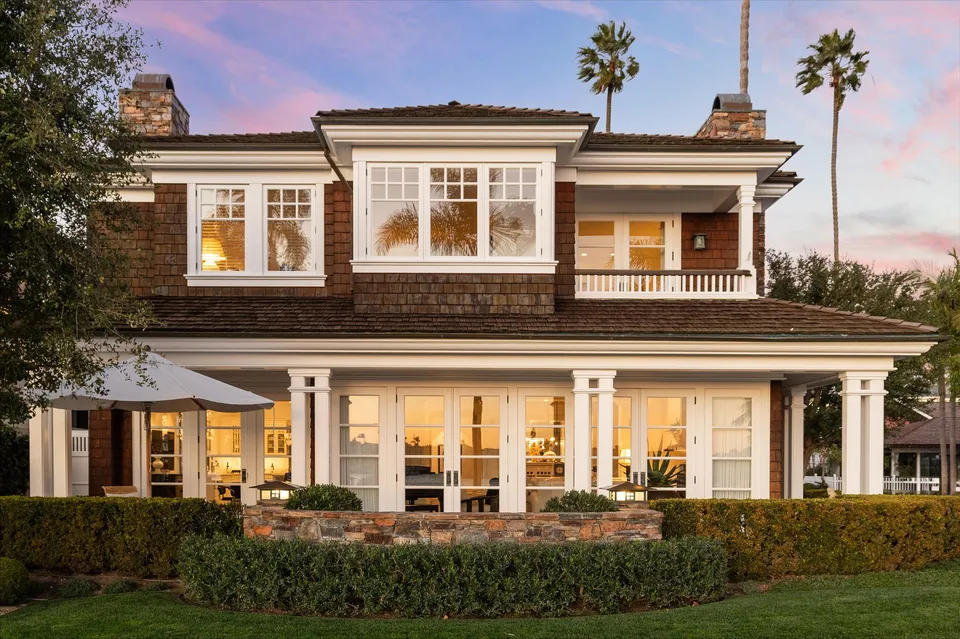 Shingle-style home with a covered porch at sunset